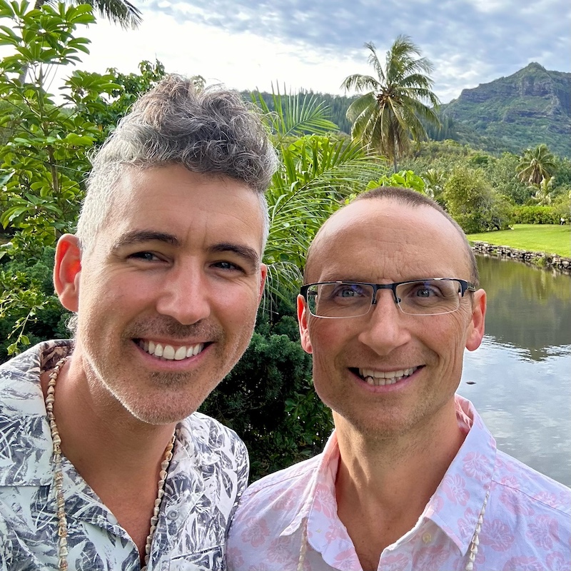 Two men standing next to each other with tropical flora and mountain behind them