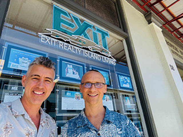 two men standing in front of a window with real estate listings behind them